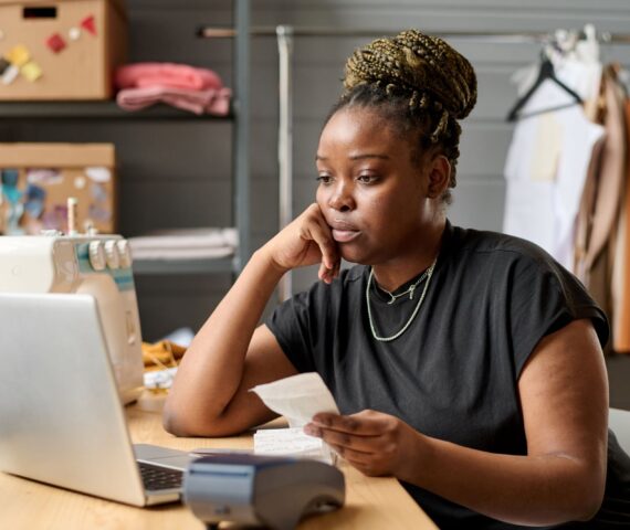 Young serious black woman with receit looking at laptop screen by workplace-tax obligations and deadlines in Kenya for business owners